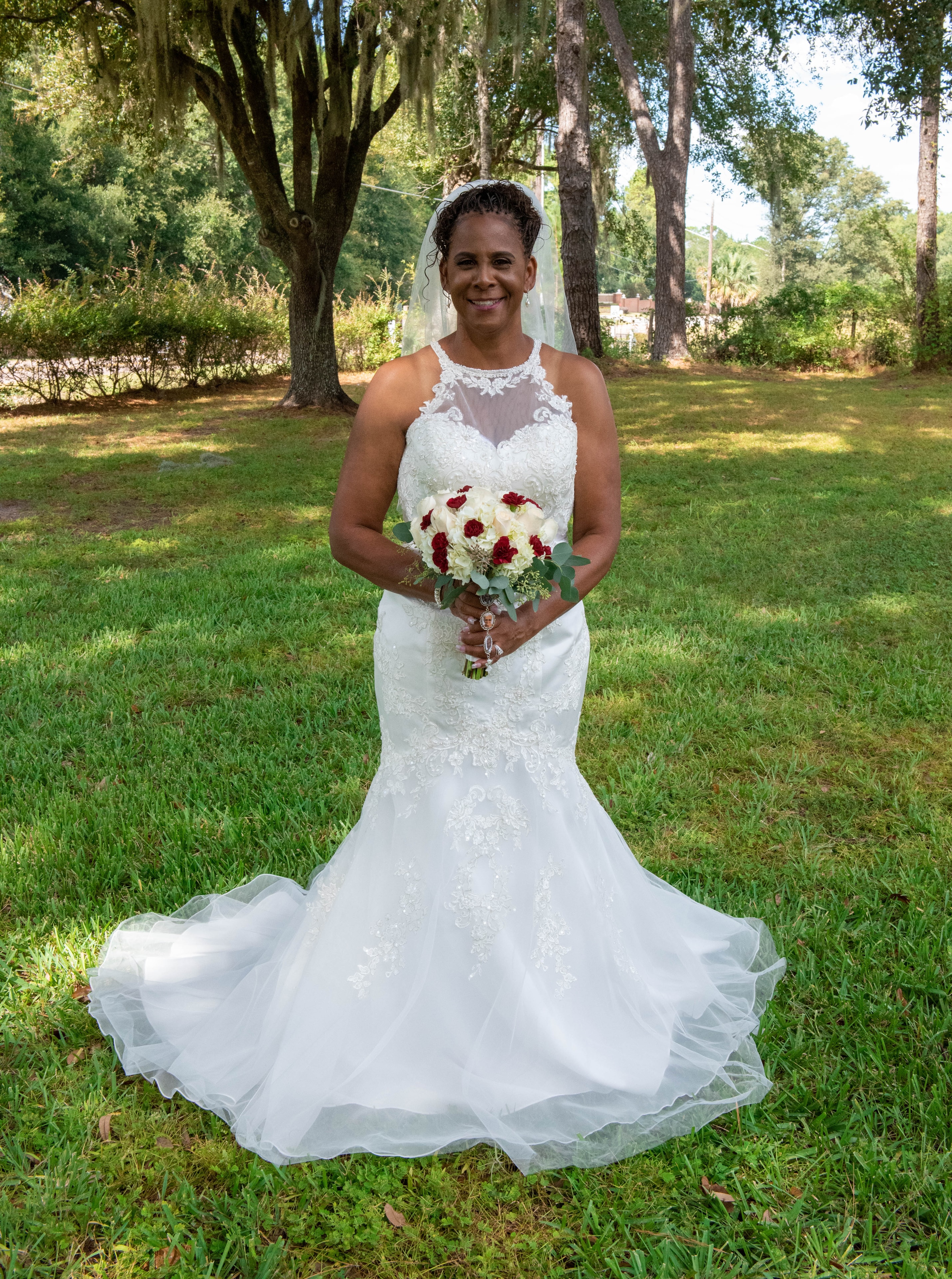 Bride in lace gown holding red and white bouquet outdoors