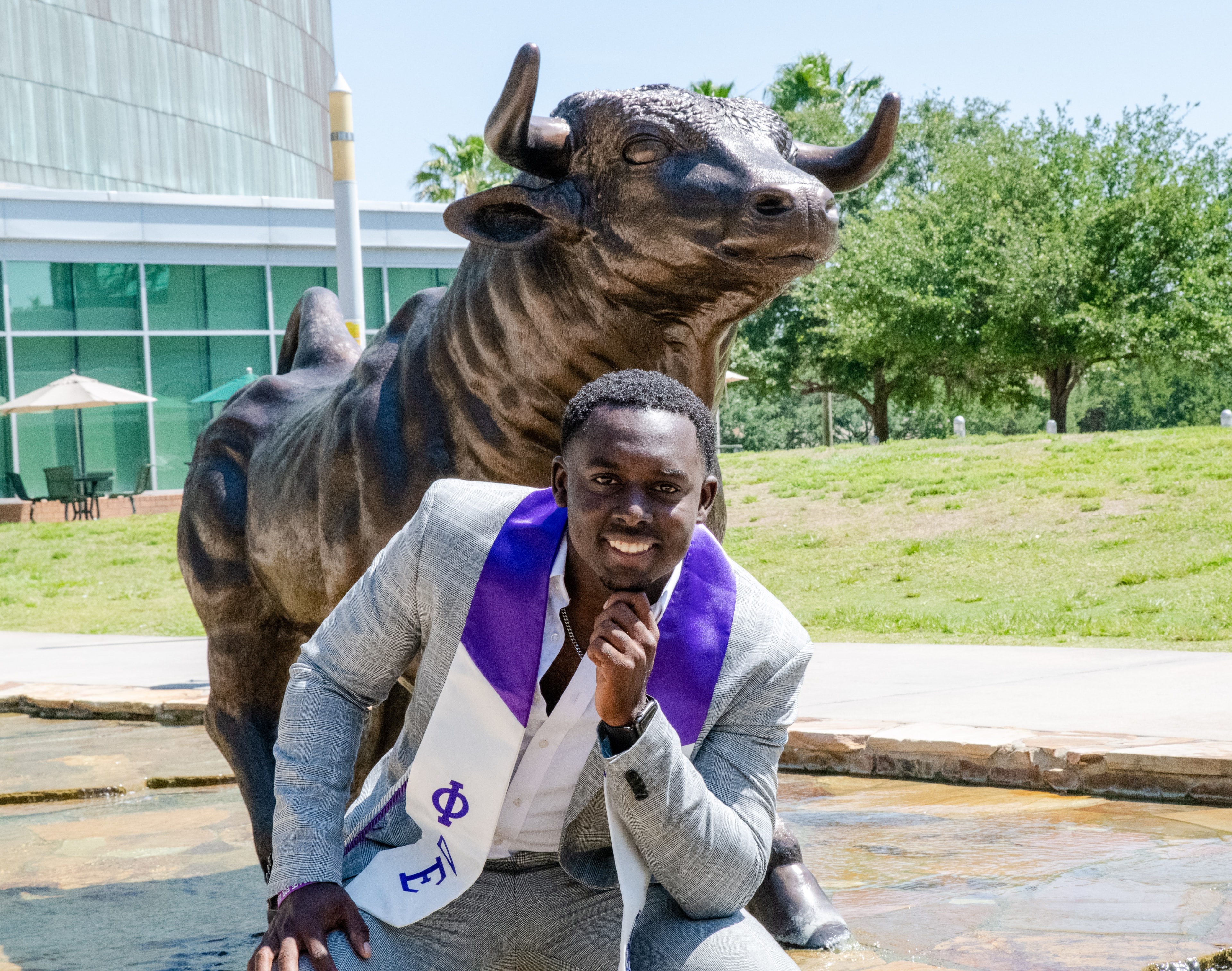 Graduate with purple stole posing in front of bull statue