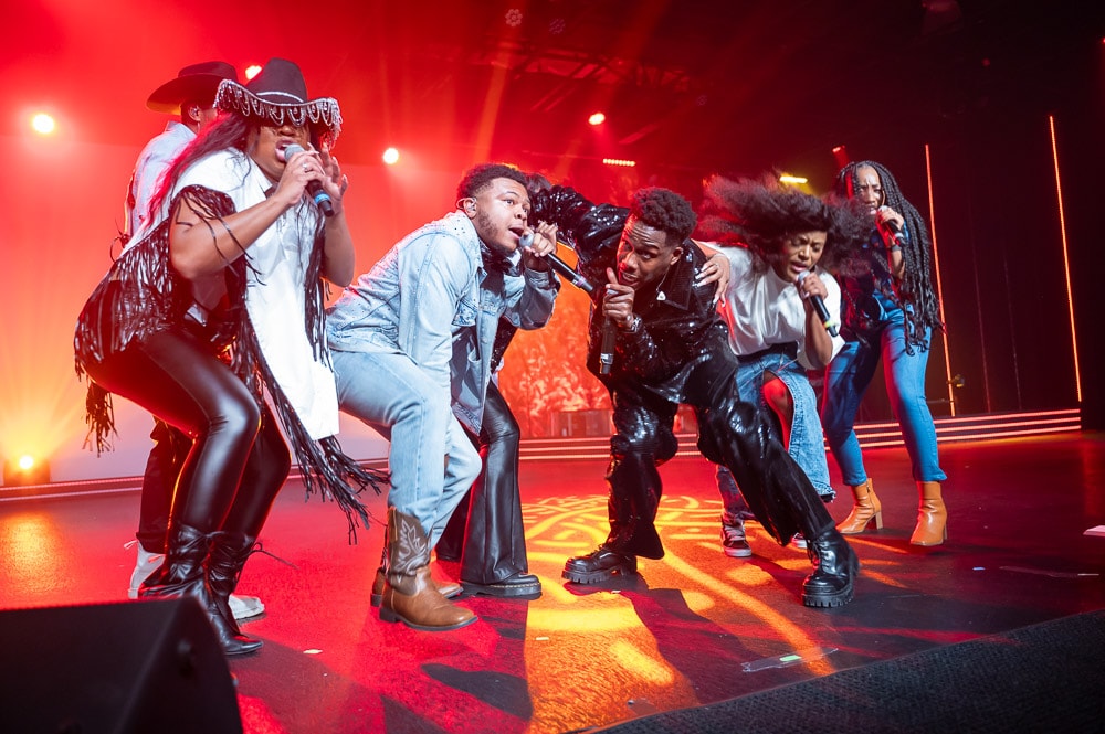 Energetic group of performers on stage under red and orange lights