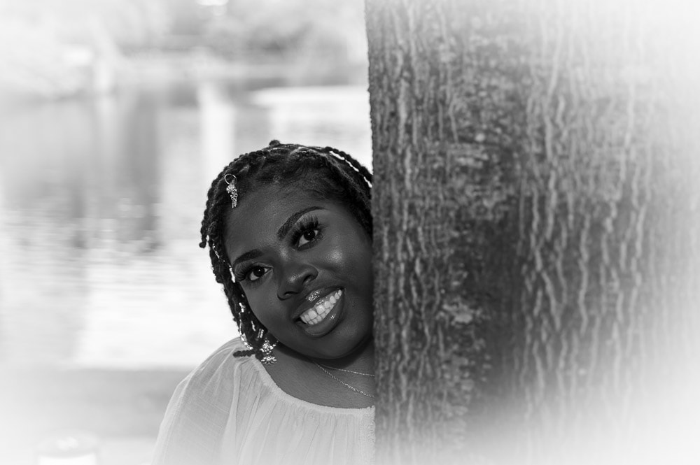 Black and white portrait of young woman peeking around a tree