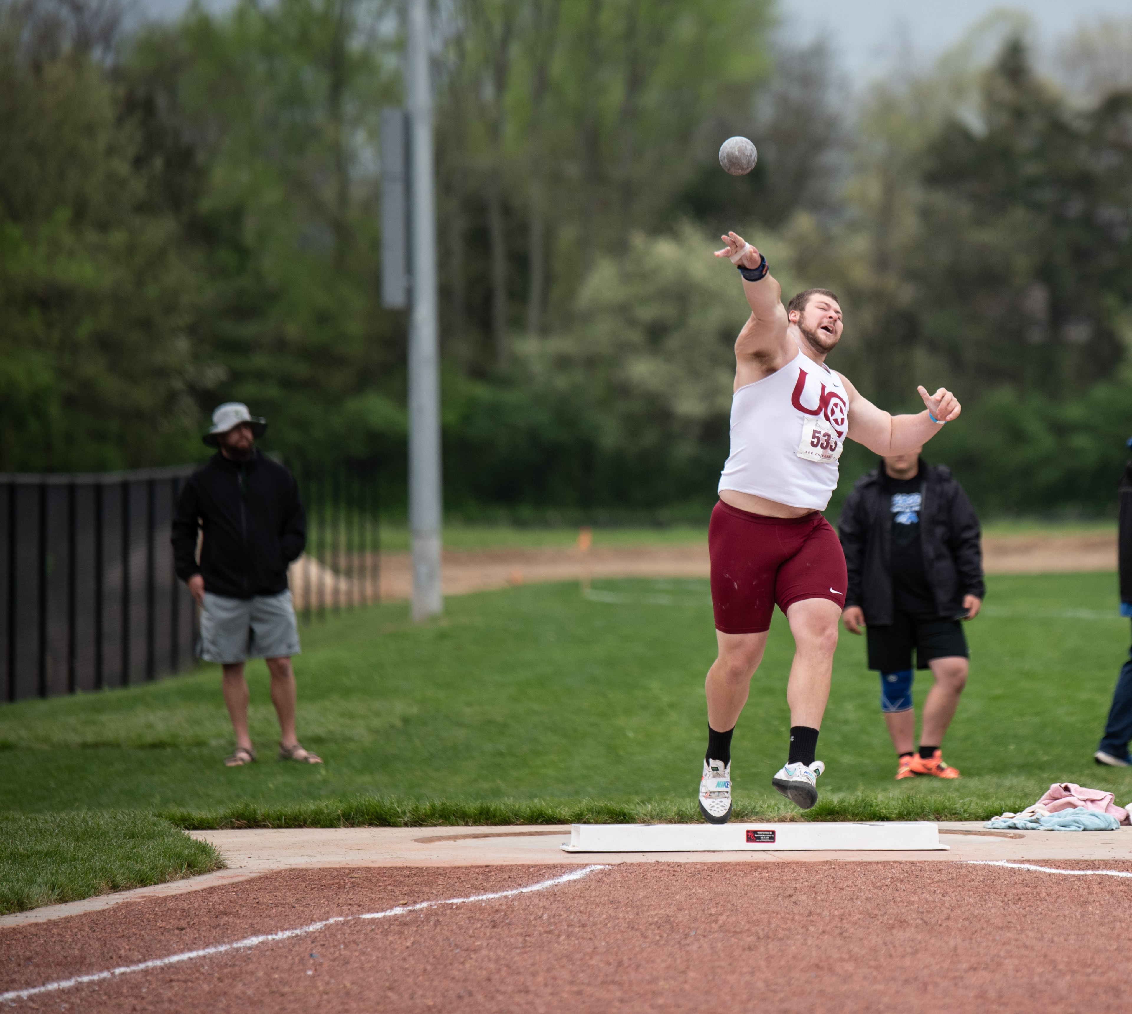 Shot put athlete releasing the ball mid-air at track meet