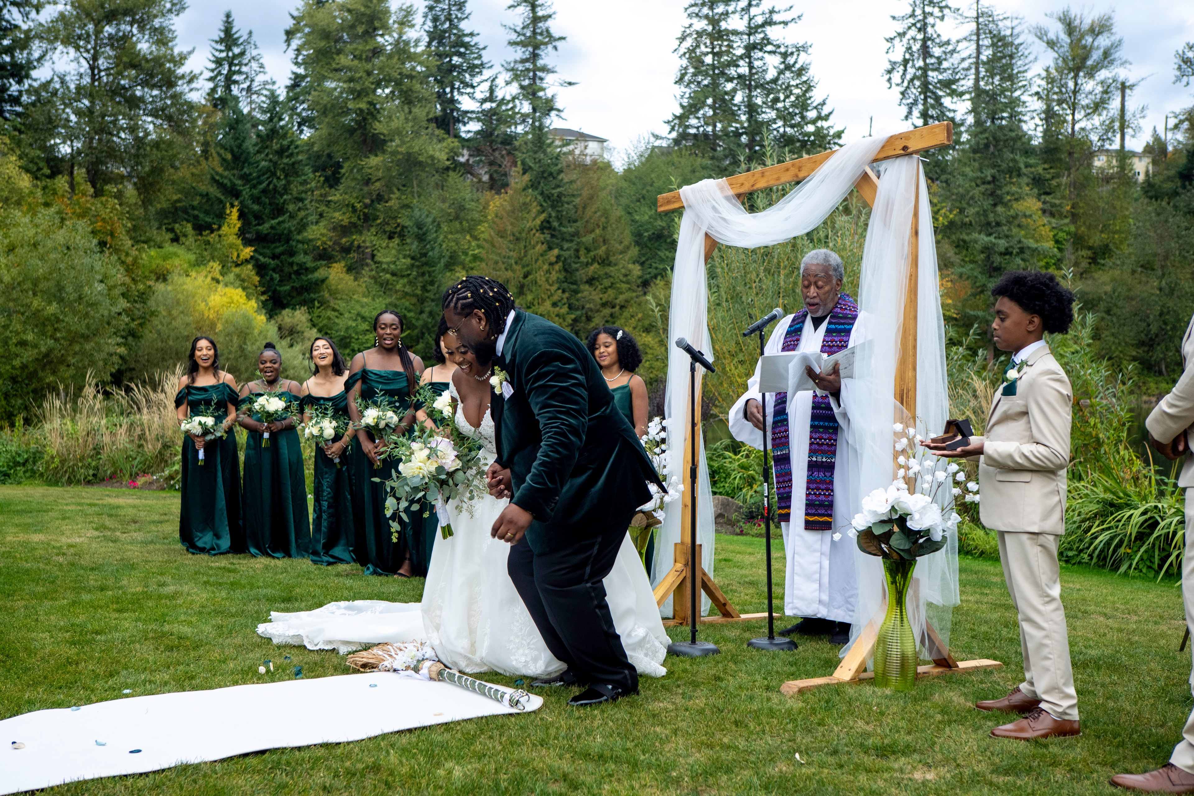 Bride and groom jumping the broom at outdoor forest wedding ceremony